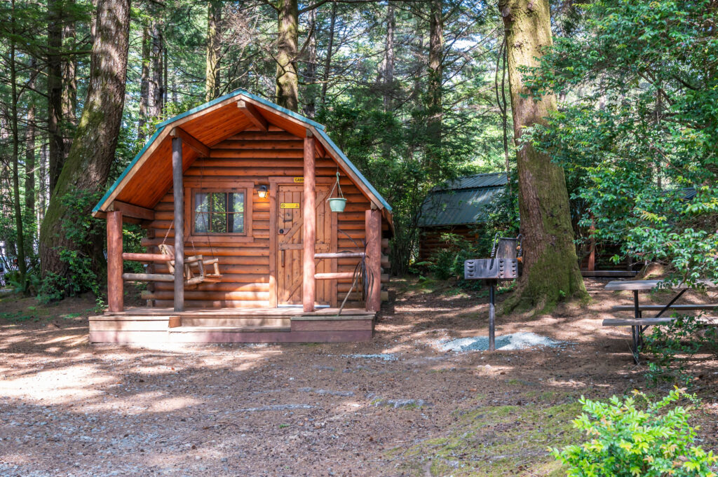outside view of a log cabin in a small clearing in the woods with a cabin seen behind it to the right