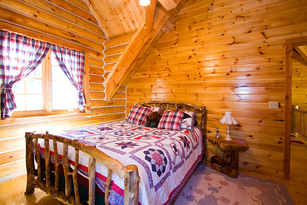 bedroom in log cabin with a rustic style bed and night stand. the bed as a stuffed moose plushie on it
