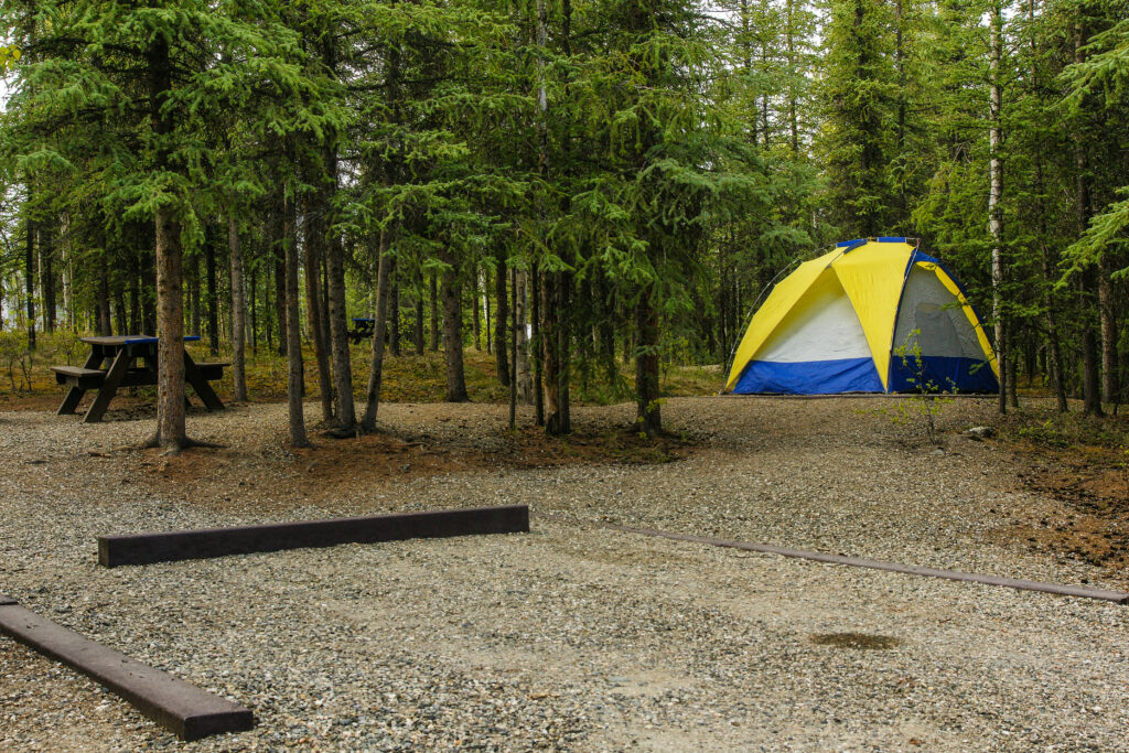 camp ground in woods with yellow, white, and blue tent and a picnic table